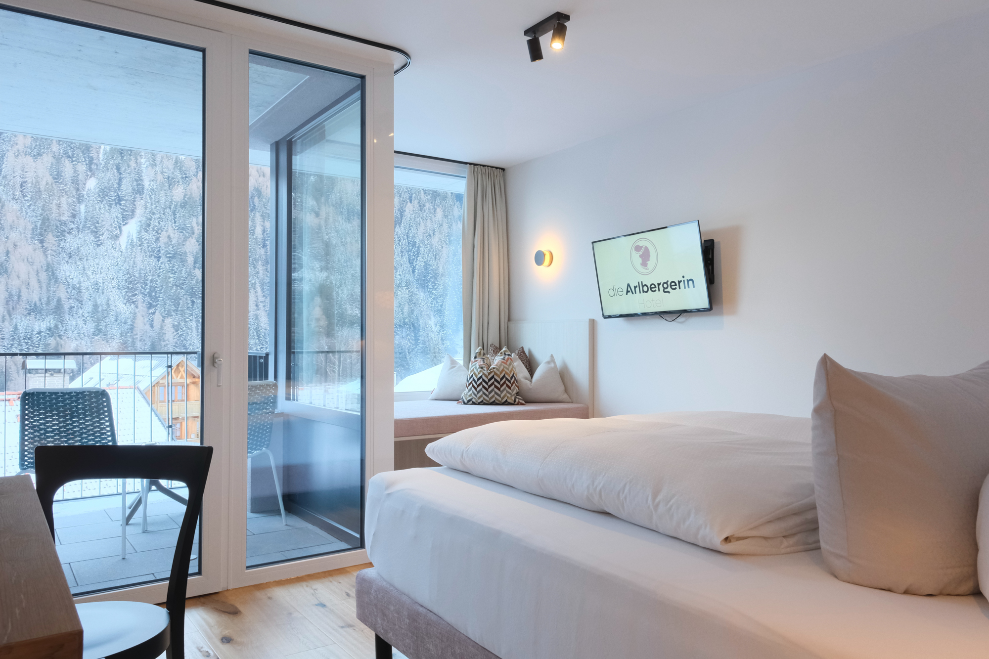 Helles, gemütliches Hotelzimmer mit Doppelbett, Holzmöbeln, Schreibtisch und großen Fenstern mit malerischem Blick auf die Berge.