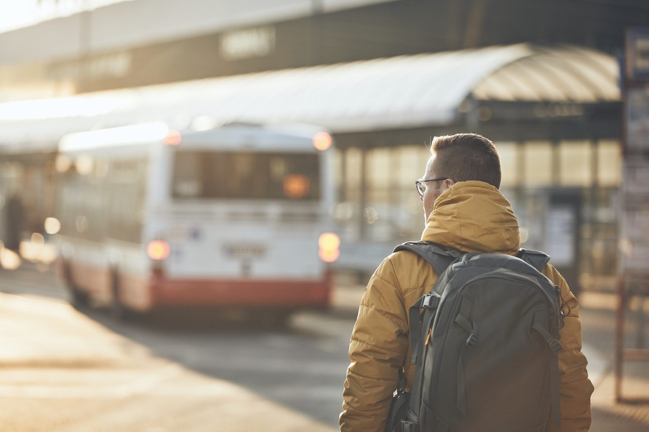 A man with a backpack stands in front of a bus, preparing to board or waiting for his journey to begin.